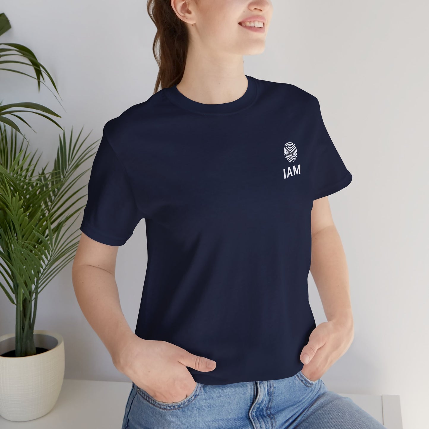 Person wearing a navy blue t-shirt with 'IAM' logo, standing indoors next to a plant.