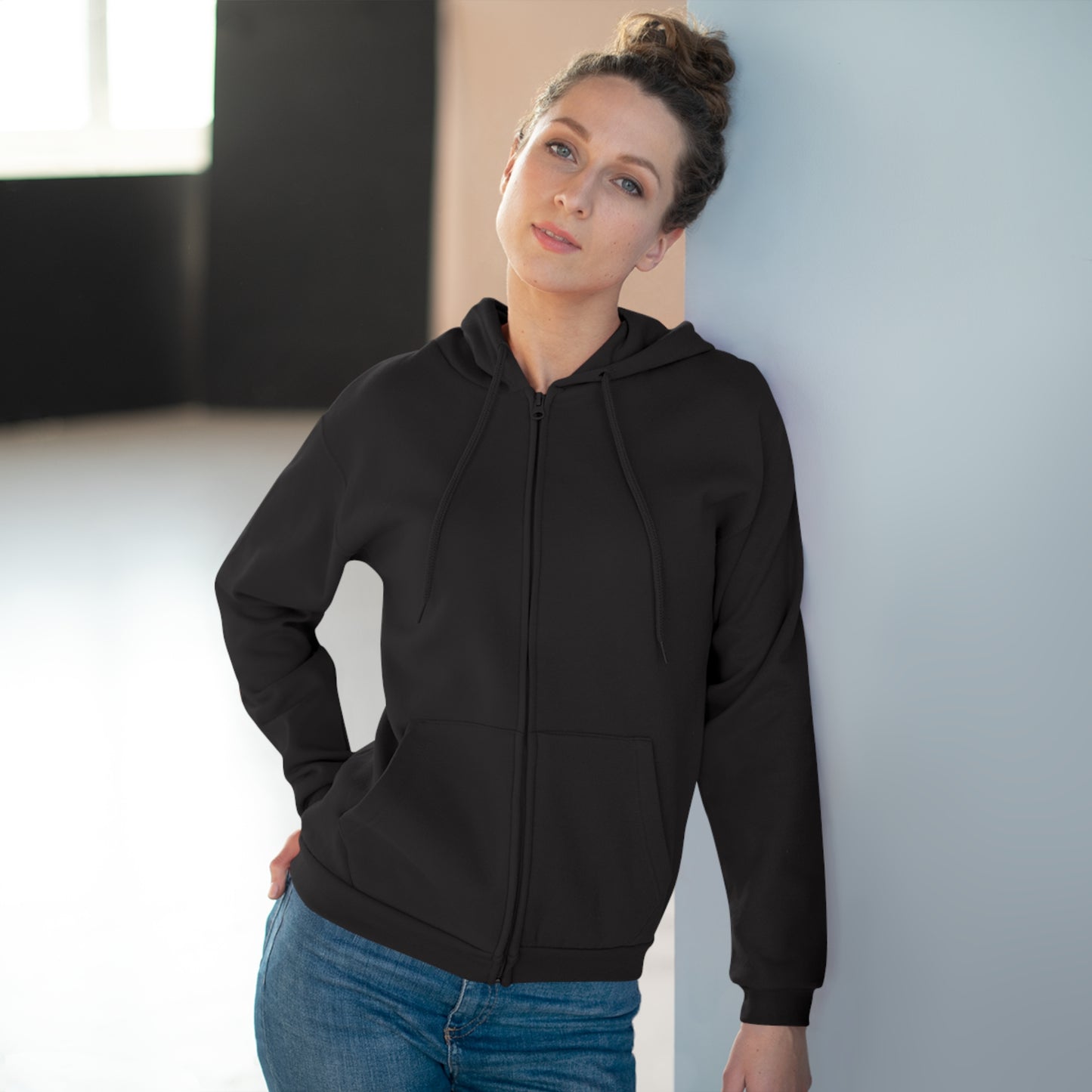 Woman wearing a black hoodie and blue jeans against a neutral background