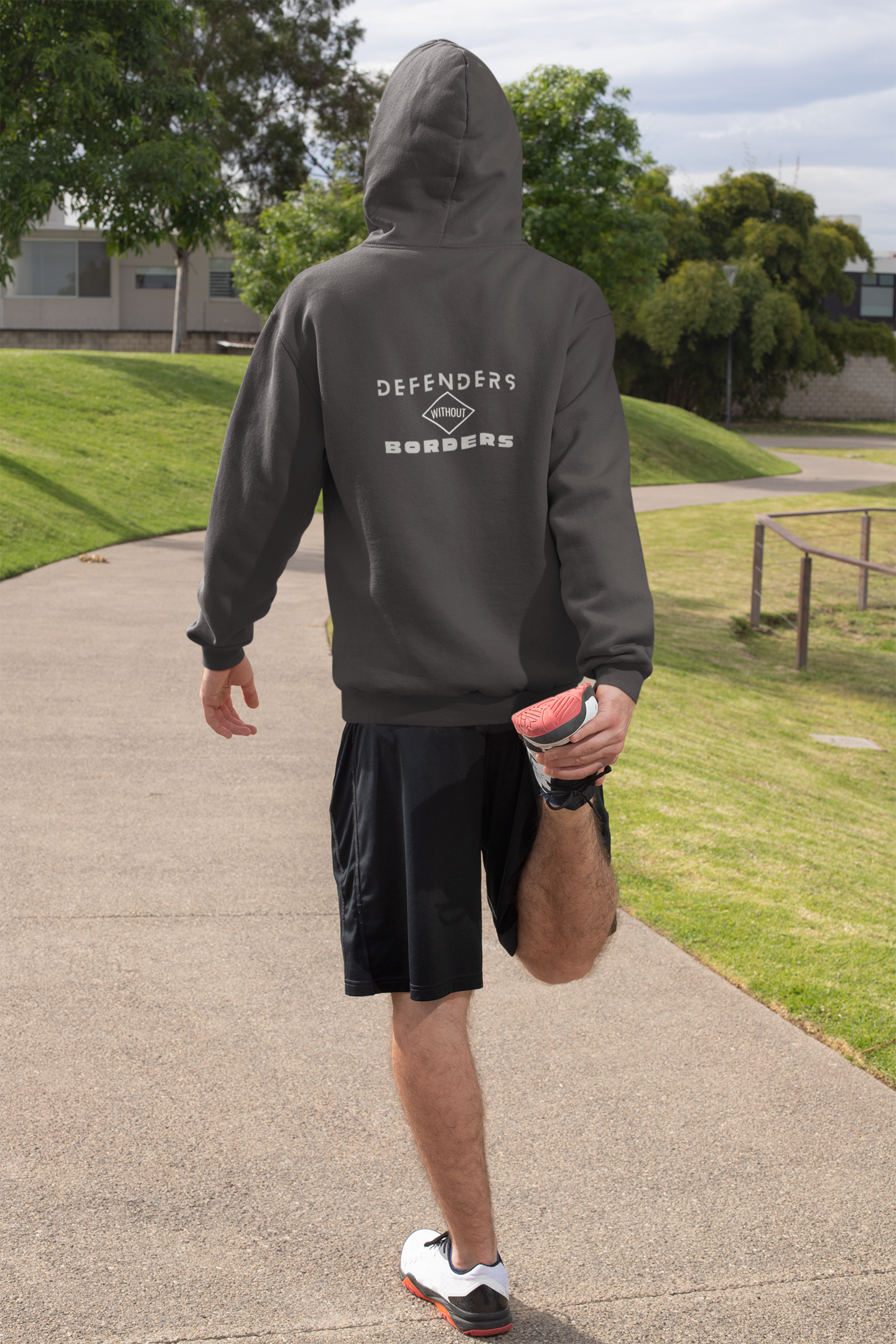 Person wearing a gray hoodie with 'DEFENDERS' branding on a park path.