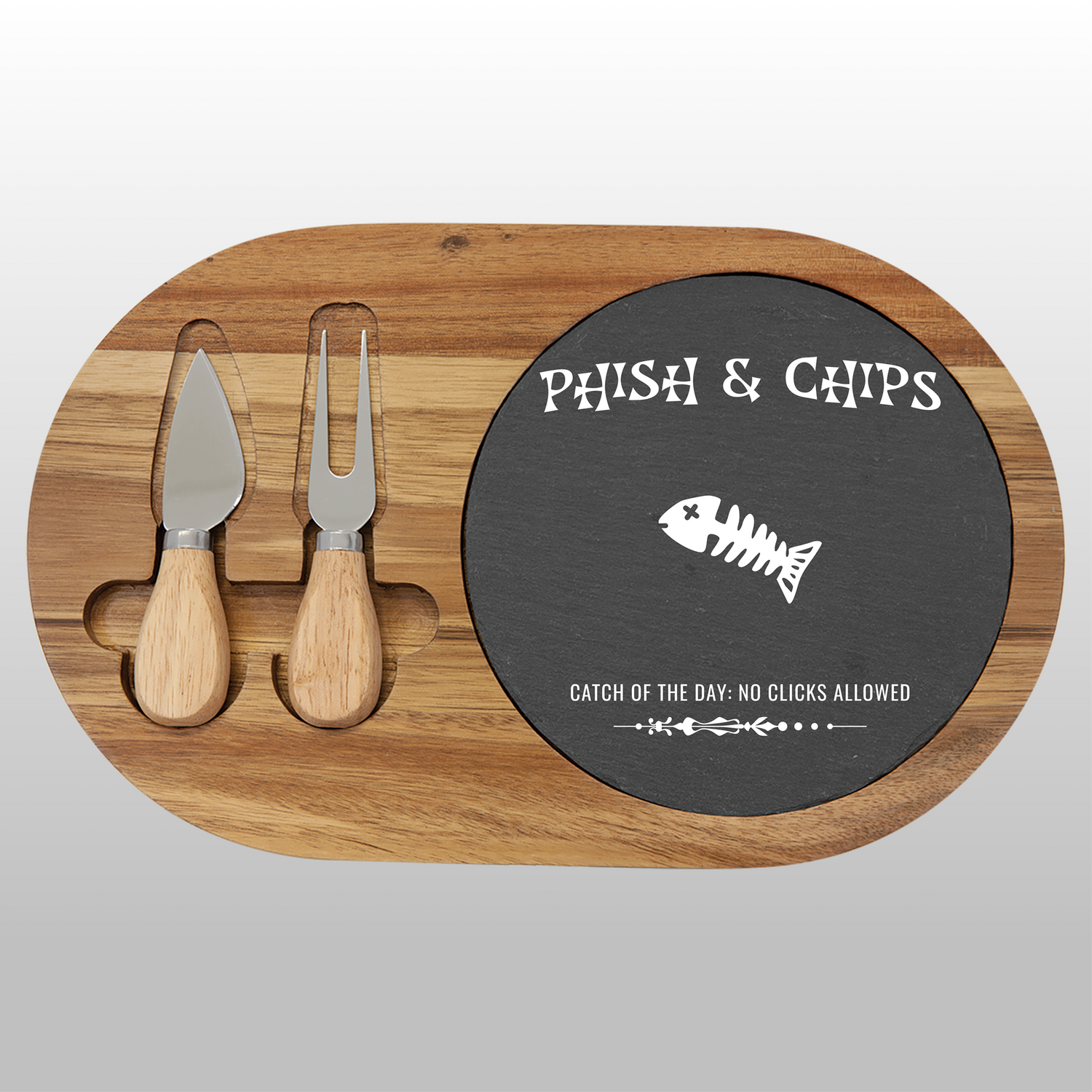 Wooden charcuterie board with cheese tools and a black round slate insert with text and fish skeleton graphic.