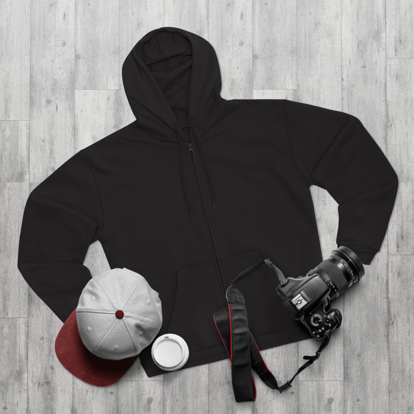 Black hoodie, white cap with red button, white mug, and camera on a wooden surface