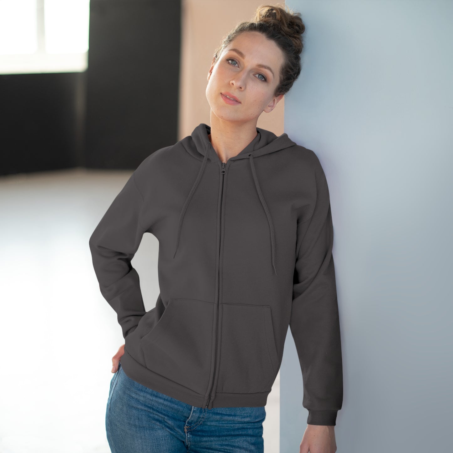 Woman wearing a gray hoodie and blue jeans against a neutral background