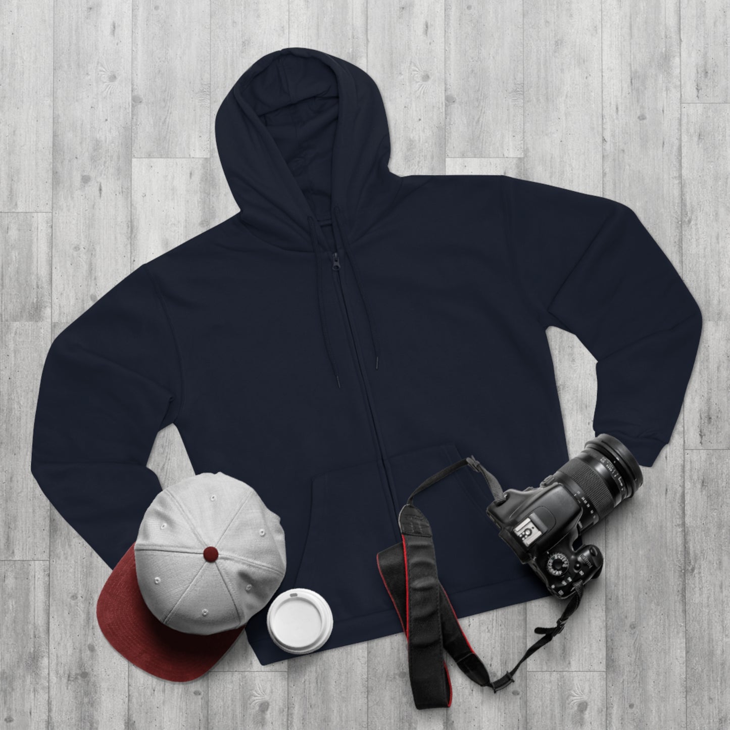 Navy hoodie, white cap, red hat, white mug, and camera on a wooden surface
